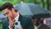 a man in a suit is covering his face with his hand while holding a cell phone