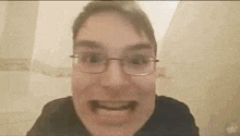 a man wearing glasses and a black shirt is making a funny face in a bathroom .