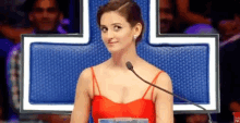 a woman in a red dress is speaking into a microphone in front of a crowd
