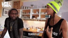 a man and a woman are standing in a kitchen and the woman is wearing a tank top that says paris