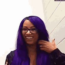 a woman with purple hair and glasses is smiling while holding her hair .