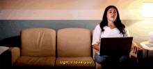 a woman is sitting on a couch with a laptop and saying ugh i love you