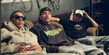 a man wearing a michigan sweatshirt sits between two other men