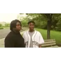 two men are standing next to each other in a park . one of the men is wearing a baseball uniform .