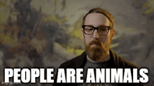 a man with a beard and glasses is standing in front of a wall and says `` people are animals '' .