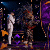 a man in a white suit is singing into a microphone while standing next to a leopard costume