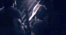 a man is playing a guitar in a dark room while another man stands behind him .