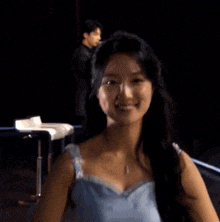 a woman in a blue dress is smiling while a man sings into a microphone in the background .