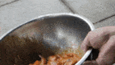 a person is holding a spoon in a metal bowl of food .