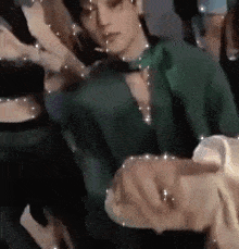 a man in a green shirt and tie is holding a woman 's hand in a crowd .