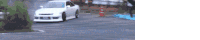 a white car is driving down a road with a red cone in the background .