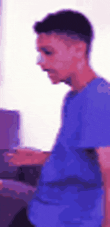 a young man in a purple shirt is standing in front of a computer .