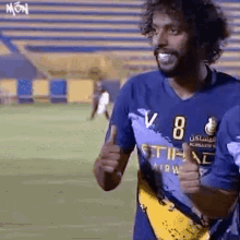 a man in a blue shirt is giving a thumbs up while standing on a soccer field .