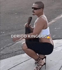 a man wearing high heels and a white tank top is squatting down on a sidewalk