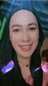 a woman wearing a hijab is smiling and looking at the camera with a blue light behind her