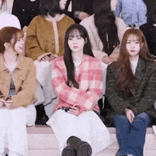 a woman in a pink plaid jacket is sitting in a crowd of people