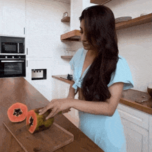 a woman in a blue dress cuts a papaya on a cutting board