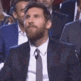 a man with a beard in a suit and tie is sitting in a crowd of people .
