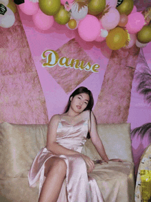 a girl in a pink dress sits on a couch in front of a banner that says danuse