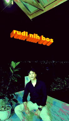 a man is sitting in front of a yellow background that says rudi nih bos