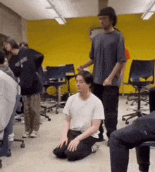 a man is kneeling down in front of a group of people in a room with a yellow wall .