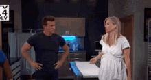 a man and a woman are standing next to each other in a kitchen . the woman is pregnant .