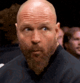 a bald man with a beard looks to the side