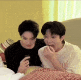 two young men are laying on a bed and one of them is eating