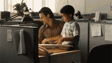 a man and a boy sit at a desk in an office cubicle