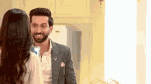 a man in a suit is standing next to a woman in a room and smiling at her .