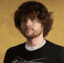 a man with curly hair and a beard is wearing a black shirt .