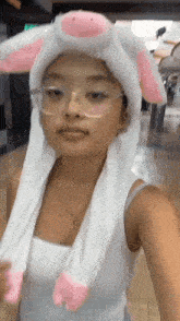 a woman wearing a white bunny hat with pink ears and glasses is taking a selfie .