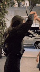 a woman in a black jacket is holding a person 's hand in front of a silver car .
