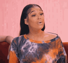 a woman in a tie dye shirt is sitting on a couch and making a funny face