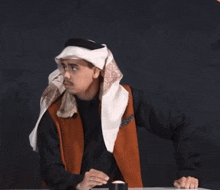 a man wearing a head scarf is sitting at a desk