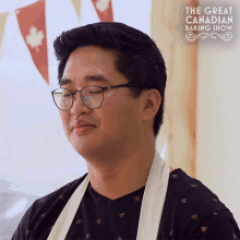 a man wearing glasses is standing in front of a sign that says " the great canadian baking show "
