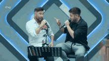two men singing into microphones in front of a rtv logo