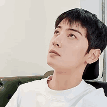 a young man is sitting on a couch wearing a white shirt and looking up .