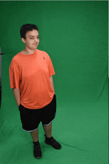 a man wearing an orange reebok shirt stands in front of a green background