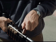 a man wearing a watch holds a shotgun in his hand