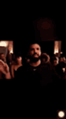 a man with a beard is standing in front of a crowd in a dark room .