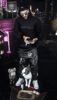 a man wearing a hoodie that says essentials is standing next to a dog