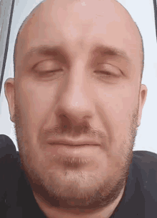 a bald man with a beard is looking at the camera with his eyes closed