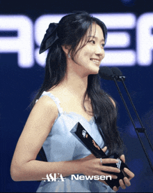 a woman in a blue dress is holding a trophy in front of a newsen sign
