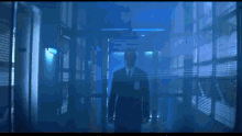 a man in a suit and tie is walking through a dark hallway with blinds .