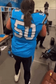 a football player wearing a blue jersey with the number 50 on it is walking in a locker room .