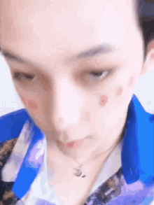 a close up of a person 's face with a blue shirt and a necklace