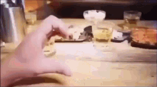 a person 's hand is reaching for a cell phone on a table with a glass of beer .