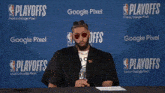 a man sits at a table in front of a wall that says playoffs
