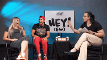 three people are sitting in front of a sign that says hey ew